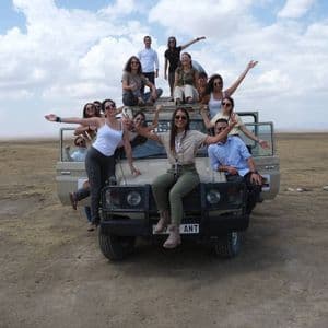 Un gruppo WeRoad sorride e posa per una foto sulla loro jeep da safari in un ampio paesaggio di savana.