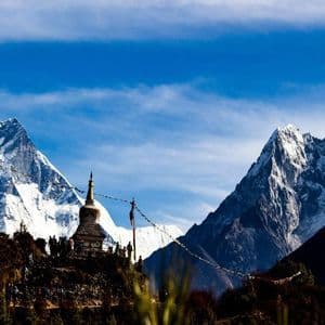 Eine WeRoad Gruppenreise steht bei einer Stupa auf einem Bergpfad, mit hohen, schneebedeckten Gipfeln vor blauem Himmel.
