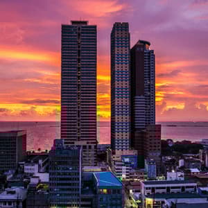 Hohe Wolkenkratzer überblicken eine Küstenstadt unter einem dramatischen pink-orangen Sonnenuntergangshimmel.