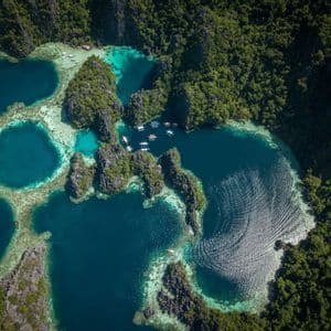 Eine Luftaufnahme kleiner Boote, die in einer türkisfarbenen Lagune ankern, umgeben von üppig grünen Felseninseln und Korallenriffen.