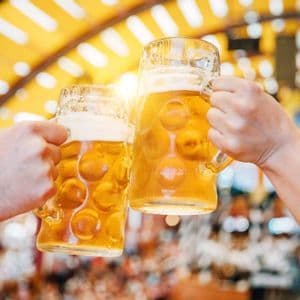 Due mani che brindano con grandi boccali di birra, su uno sfondo sfocato e ben illuminato.