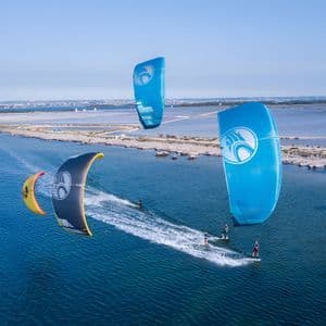 Vista aerea di un viaggio di gruppo WeRoad che fa kitesurf con aquiloni colorati su un mare calmo e blu.
