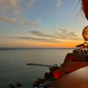 Vista da un ristorante sulla scogliera con affaccio sul mare durante un tramonto colorato, con una lanterna ornata in primo piano.