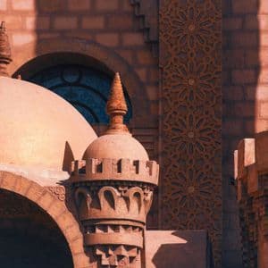Primo piano di architettura color terracotta, ornata con cupole, minareti e intagli geometrici intricati, sotto la luce del sole.