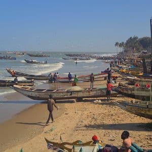 Ein belebter Sandstrand mit vielen Menschen und bunten hölzernen Fischerbooten am Ufer und in den sanften Wellen unter klarem Himmel.