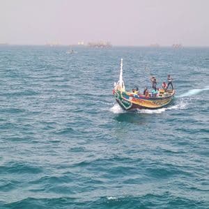 Eine Gruppe von Menschen auf einem farbenfrohen Holzboot segelt über ein unruhiges blaues Meer, mit weiteren Booten in der diesigen Ferne.