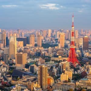 An aerial view of a dense cityscape with a prominent red and white tower illuminated by the warm light of sunset.