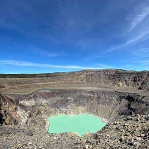 Ein Blick vom Rand eines großen Vulkankraters mit einem türkisfarbenen See unter klarem blauem Himmel.
