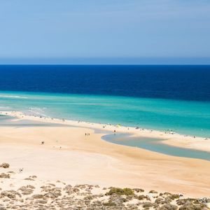 Eine Luftaufnahme eines Sandstrandes, an dem Menschen entlang der türkisfarbenen Küste verstreut sind, mit dem tiefblauen Ozean im Hintergrund.