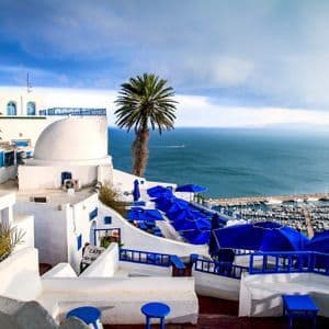 Des bâtiments blanchis à la chaux avec des détails bleus éclatants et des parasols surplombent une marina côtière remplie de bateaux.