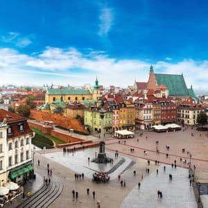 Una vista elevada de una plaza histórica europea llena de gente, rodeada de edificios coloridos y catedrales bajo un cielo azul.