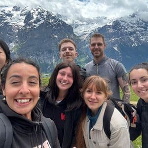 Un groupe WeRoad prend un selfie souriant avec une chaîne de montagnes enneigée en arrière-plan.