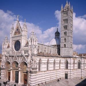 Una cattedrale ornata con un motivo a strisce bianche e scure sulla sua facciata e un alto campanile, vista dall'alto sotto un cielo azzurro.