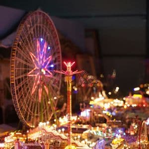 Maqueta en miniatura de un parque de atracciones iluminado de noche, con noria y columpio gigante en primer plano.