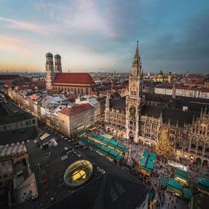Una vista aérea de un animado mercado navideño en una plaza de la ciudad al atardecer, con puestos, multitudes y arquitectura histórica.