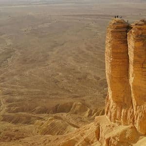 Un voyage de groupe WeRoad se tient sur une haute falaise surplombant un vaste canyon désertique sous un ciel voilé.