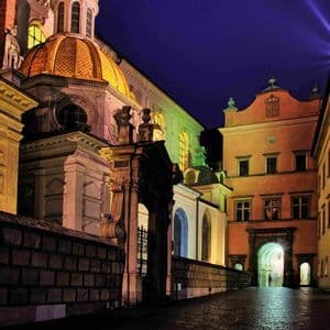 Una histórica calle empedrada de noche, con un edificio ornamentado que presenta una gran cúpula dorada iluminada contra un cielo oscuro.