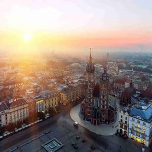 Una vista aérea de una plaza histórica y una gran iglesia de ladrillo bañadas por la luz dorada de un amanecer brumoso.