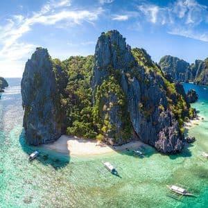 Un panorama aereo di imbarcazioni a bilanciere che galleggiano in limpida acqua turchese, vicino a una spiaggia sabbiosa incastonata tra isole verdi e rocciose.