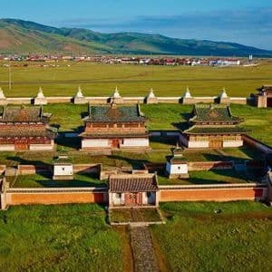 Eine Luftaufnahme eines ummauerten Tempelkomplexes mit traditionellen Gebäuden in einer weiten grünen Ebene, mit einer Stadt und Hügeln in der Ferne.