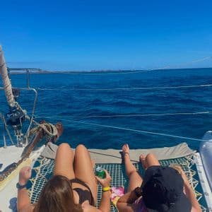 Dos mujeres de un viaje en grupo de WeRoad toman el sol en la red de un catamarán mientras navegan en el mar azul.
