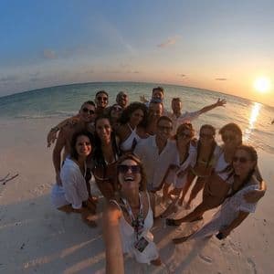Eine große WeRoad-Gruppe macht ein Selfie an einem weißen Sandstrand, während die Sonne über dem Meer untergeht.