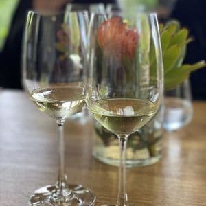 Zwei Gläser Weißwein stehen auf einem Holztisch neben einer Vase mit Blumen während einer WeRoad Gruppenreise.