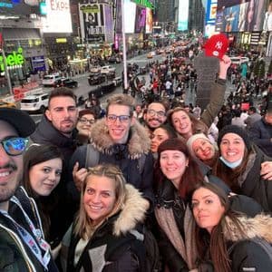 Un grupo de WeRoad se toma una selfie en unas escaleras con vistas a una animada plaza de la ciudad, llena de luminosos carteles y multitudes.