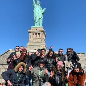 Un gruppo WeRoad in posa per una foto davanti alla Statua della Libertà sotto un cielo azzurro e limpido.