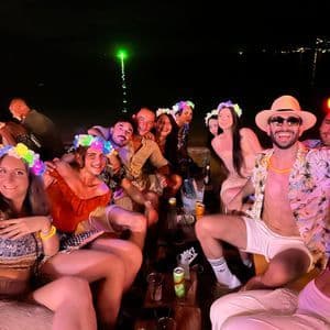 Un gruppo WeRoad posa per una foto a una festa in spiaggia notturna, indossando cerchietti floreali luminosi e festosi.