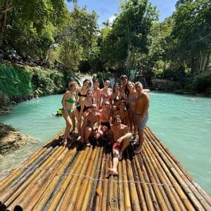 Un viaggio di gruppo WeRoad con persone in costume da bagno che posano insieme su una grande zattera di bambù, su un fiume turchese in una foresta lussureggiante.