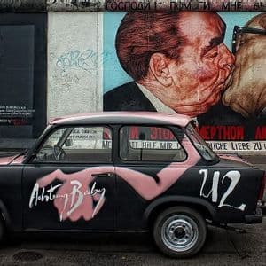 Un Trabant negro pintado con "Achtung Baby" está aparcado frente al mural "Beso Fraternal" en el Muro de Berlín.