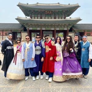 Un viaggio di gruppo WeRoad in posa con colorati abiti tradizionali coreani davanti a un grande cancello tradizionale di un palazzo asiatico.