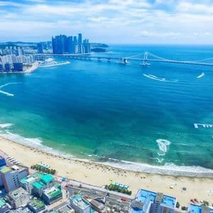 Vista aerea di una vivace città costiera con una spiaggia sabbiosa che si curva attorno a una baia, con un lungo ponte in lontananza.
