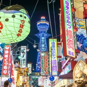 Una vivace strada giapponese di notte, illuminata da insegne al neon colorate, una grande lanterna a forma di pesce palla e una torre illuminata in lontananza.