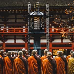 Un gruppo di monaci buddisti in tuniche arancioni si trova di fronte a un tradizionale tempio rosso durante l'autunno.