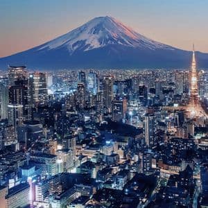 Un paesaggio urbano scintillante e una torre illuminata si stagliano di fronte a un'imponente montagna innevata al crepuscolo.