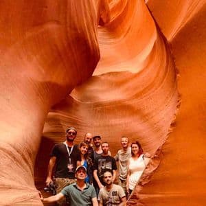 Un viaje en grupo de WeRoad posando para una foto dentro de un estrecho cañón de ranura naranja con paredes de roca lisas y onduladas.