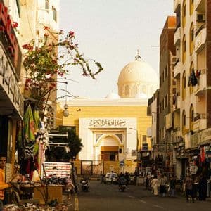 Una vista su una strada cittadina fiancheggiata da negozi, con una moschea prominente e la sua grande cupola bianca visibile sullo sfondo.
