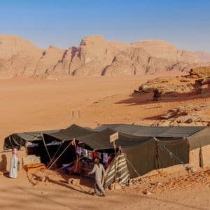 Due persone in abiti tradizionali fuori da una bancarella tendata in un deserto con grandi formazioni rocciose.