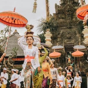 Una processione di donne in abiti tradizionali colorati porta offerte sulla testa su per i gradini di pietra verso un tempio.