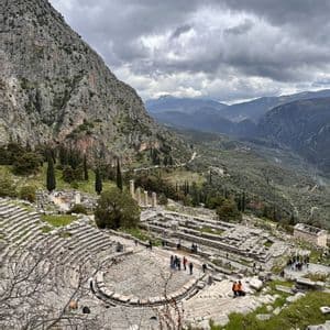 Veduta dall'alto di un antico anfiteatro in pietra e rovine incastonate nel fianco di una montagna, con un gruppo WeRoad che esplora il sito.