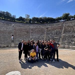 Un gruppo WeRoad posa per una foto al centro di un grande anfiteatro in pietra sotto un cielo azzurro.