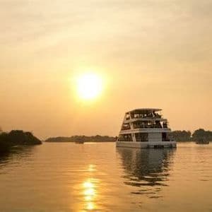 Una barca a più ponti con a bordo un viaggio di gruppo WeRoad naviga su un fiume calmo durante un tramonto dorato.