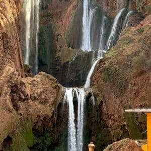Un viaggio di gruppo WeRoad ammira un'ampia cascata a più livelli che scende da scogliere di roccia rossa in una piscina naturale.