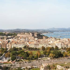 An aerial view of a historic coastal city featuring a fortress, a park, and a large cruise ship in the harbor.