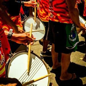 Primer plano de un viaje en grupo de WeRoad tocando tambores en camisas coloridas rojas y amarillas durante un festival callejero soleado.
