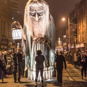 Un gigantesco burattino di una vecchia con una lanterna sfila di notte per una strada affollata della città.