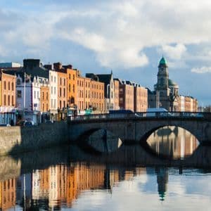 Una fila di edifici colorati e un ponte in pietra ad arco si riflettono nell'acqua calma di un fiume.