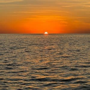 Il sole che tramonta sull'oceano, creando un intenso bagliore arancione sull'acqua e nel cielo.